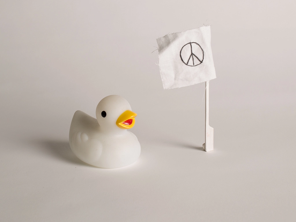 Canard en plastique blanc et son drapeau orné d’un signe de paix sur fond blanc