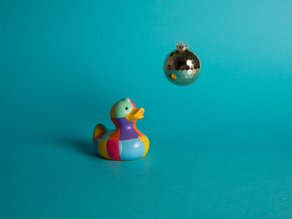 Canard en plastique à carreau multicolore et sa boule disco sur fond bleu