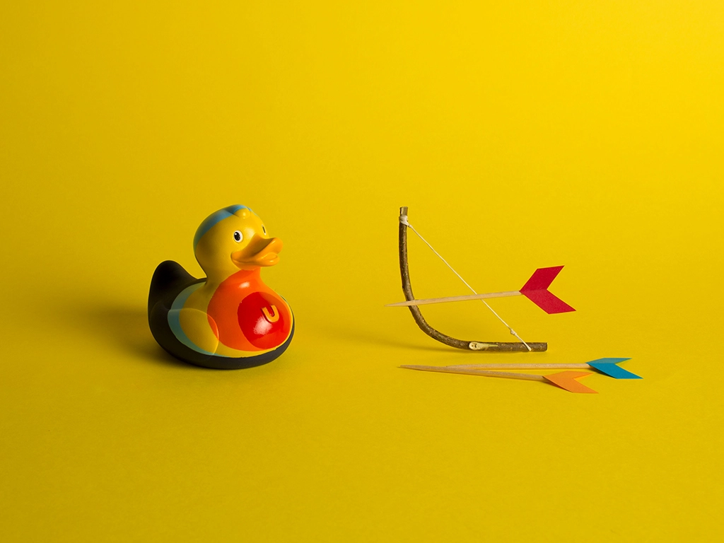 Canard en plastique à motif cible avec son petit arc en bois et ses flèches sur fond jaune